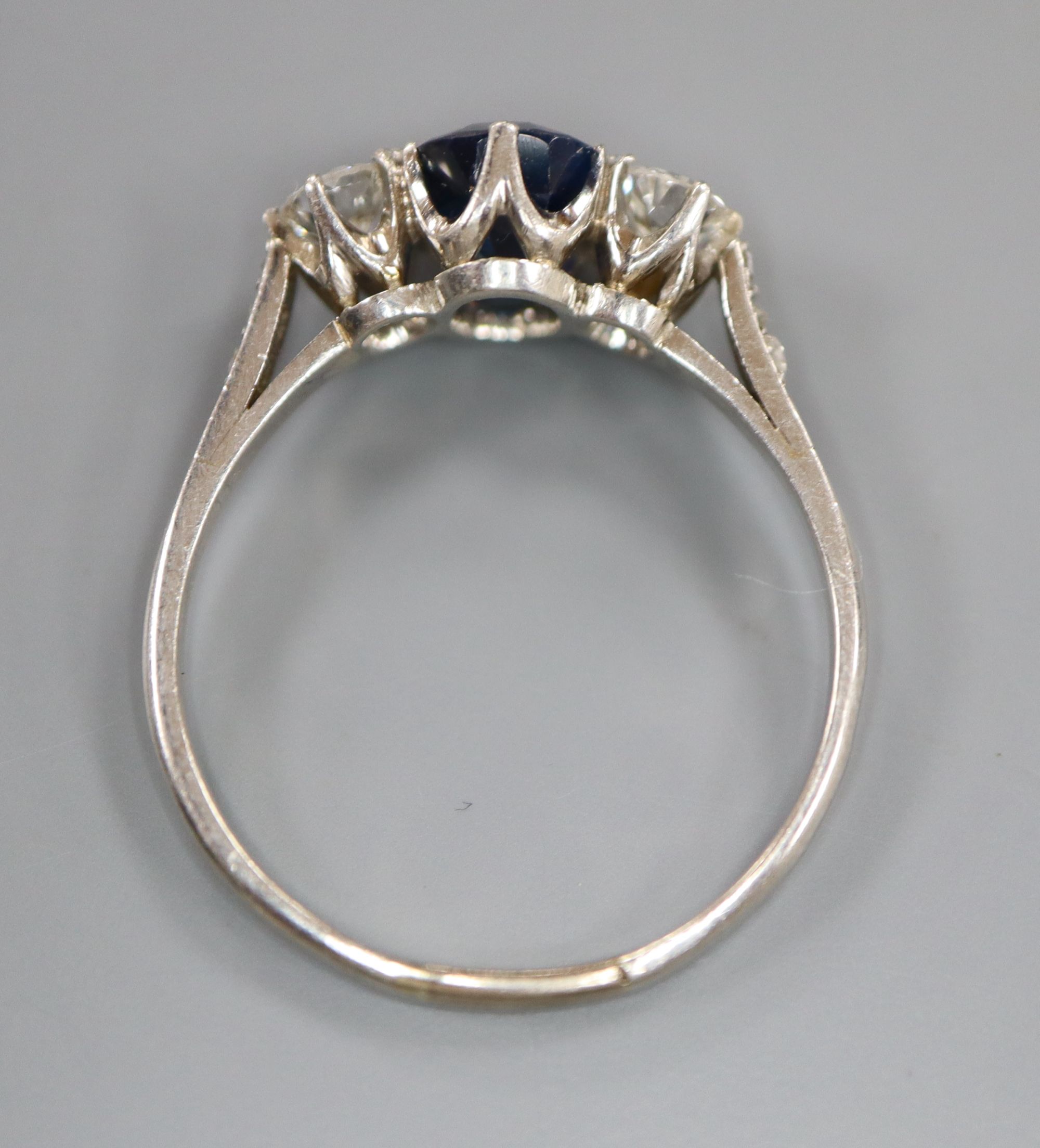 A white metal, sapphire and diamond three stone ring, with diamond chip set shoulders, size Q, gross 3.6 grams.